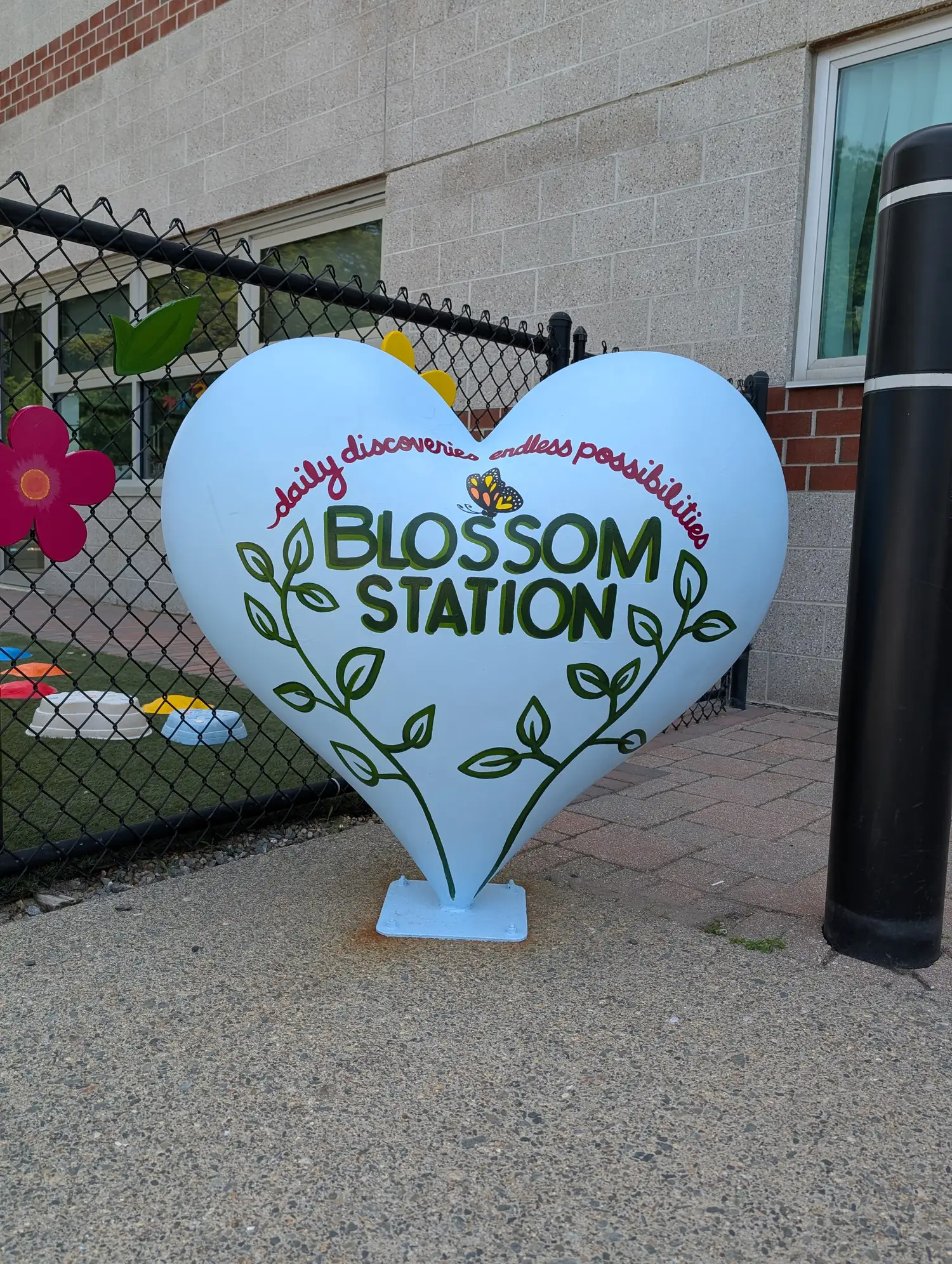 Blossom Station Child Care Center's painted heart sign reading Daily Discoveries, Endless Possibilities, at its Acton, Massachusetts playground