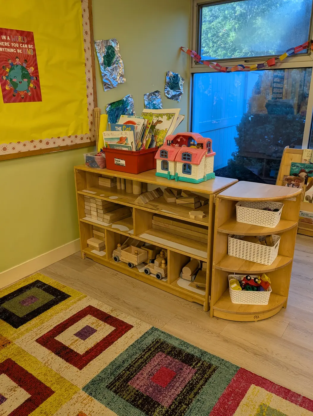 A bright block and building area with a dollhouse and wooden shelves at Blossom Station