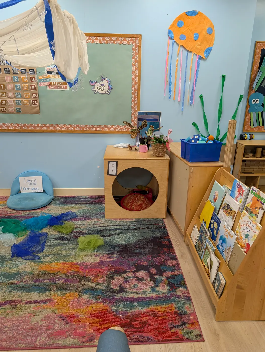 A cozy classroom reading nook with books and a colorful rug at Blossom Station