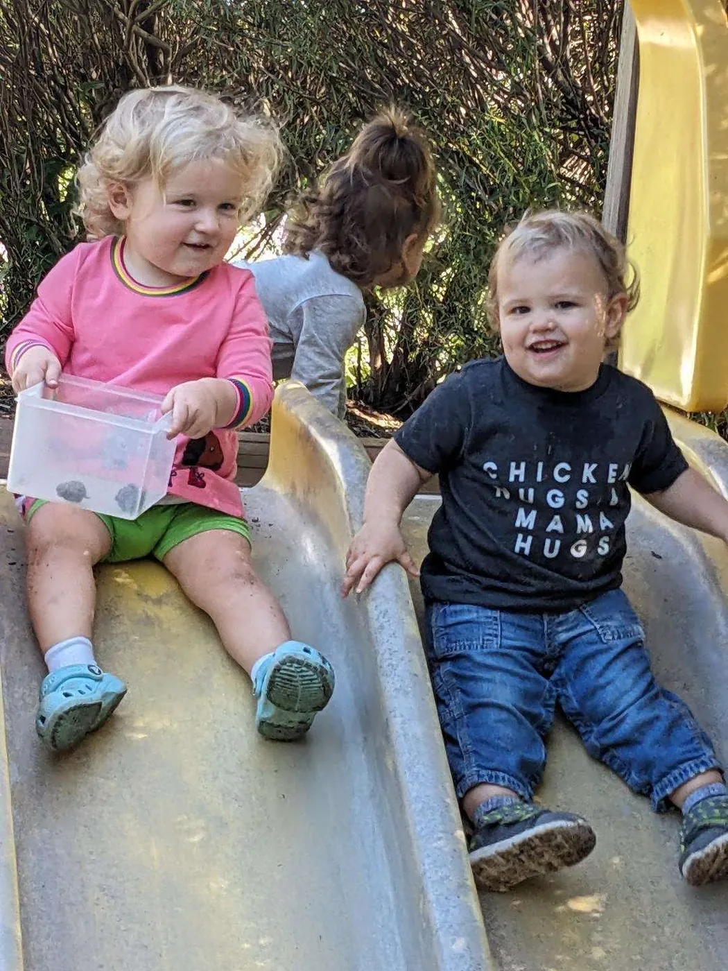 Two toddlers laughing together on the slide at Blossom Station